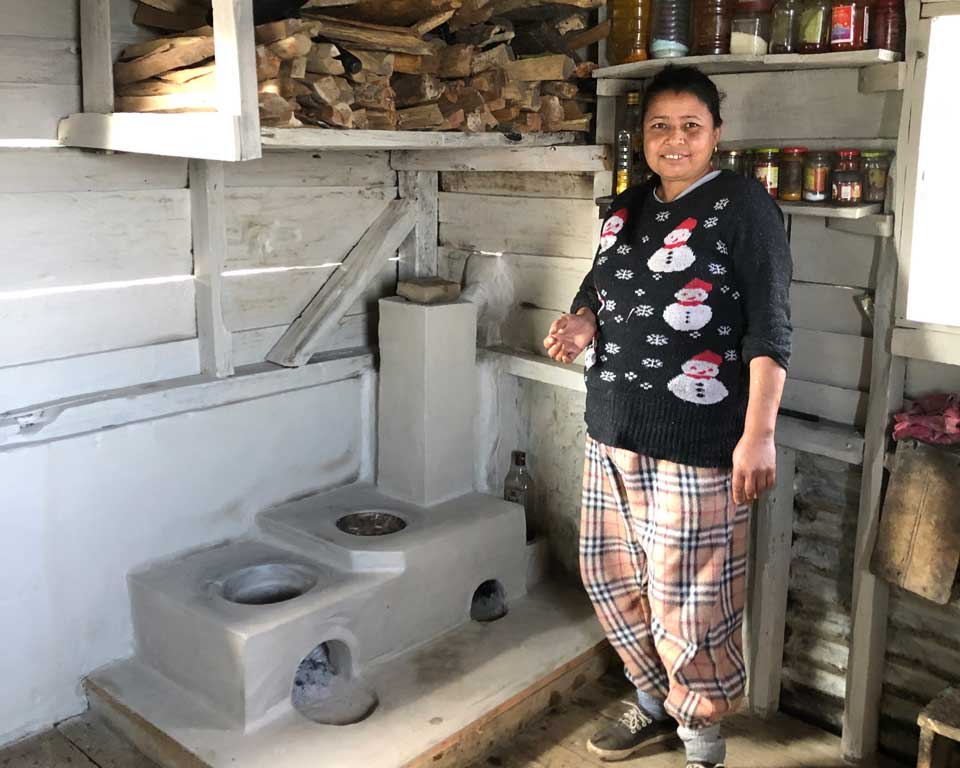 A woman standing in her kitchen with her Improved Cookstove.